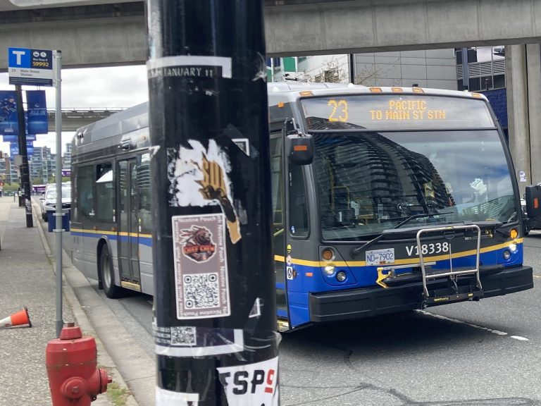 A bus at a bus stop. The Bus is a 40-foot standard bus with the headsign "23"