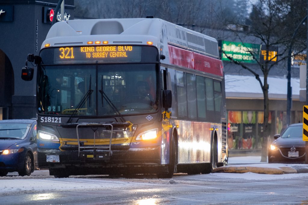 A 12 meter transit bus with its left blinker on waiting to make a turn in a snowy day,