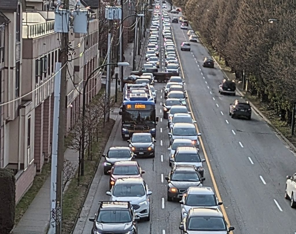 PXL_20240315_011321075~2 A picture of the 84 bus stuck in congestion on 6th. There's a massive queue of cars filling both lanes and the bus is just stuck in it.
